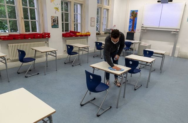 Professor desinfeta mesas da sala de aula para receber alunos na volta às aulas. Foto: iStock.