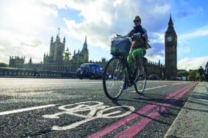 Ciclista cruzando a ponte de Westminster em ciclovia fora do Palácio de Westminster e do edifício do Parlamento da Inglaterra em Londres. Foto: London Cycling Campaign.